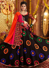 Woman in traditional black and red embroidered outfit with colorful patterns, standing against a decorative background.
